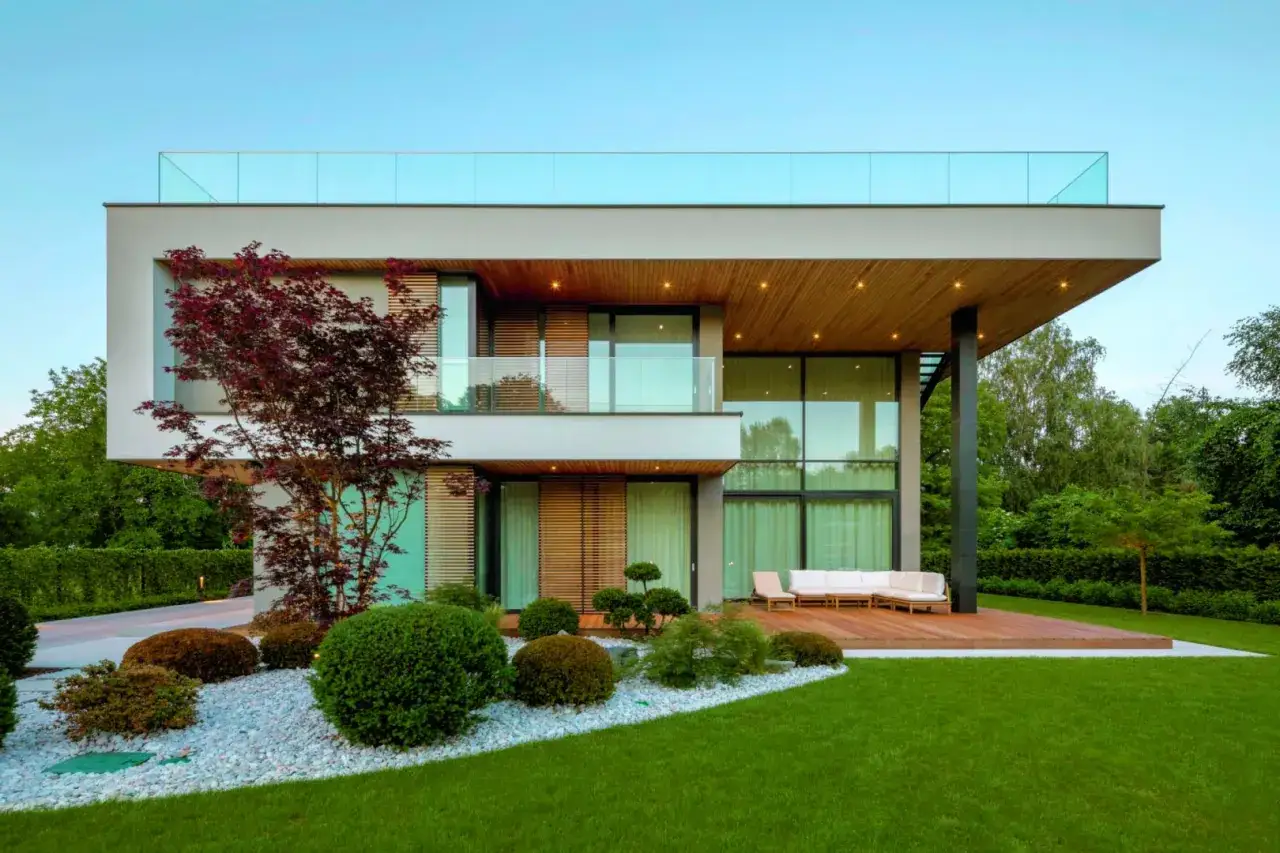 Nowoczesny dom z tarasem i lekki dach płaski, otoczony zielenią i ozdobnymi krzewami.