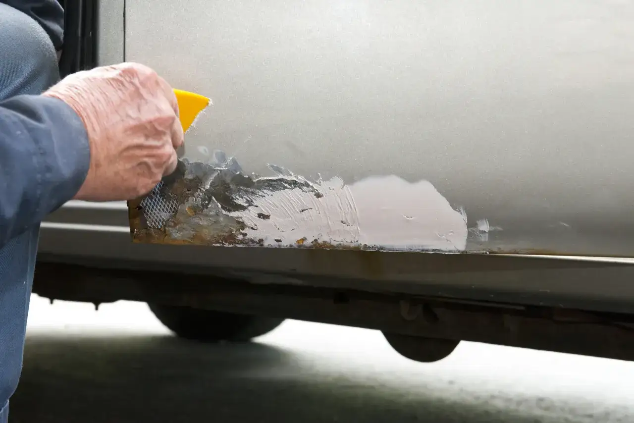 Nakładanie masy szpachlowej na zardzewiałe miejsce, by jak załatać dziurę w samochodzie.