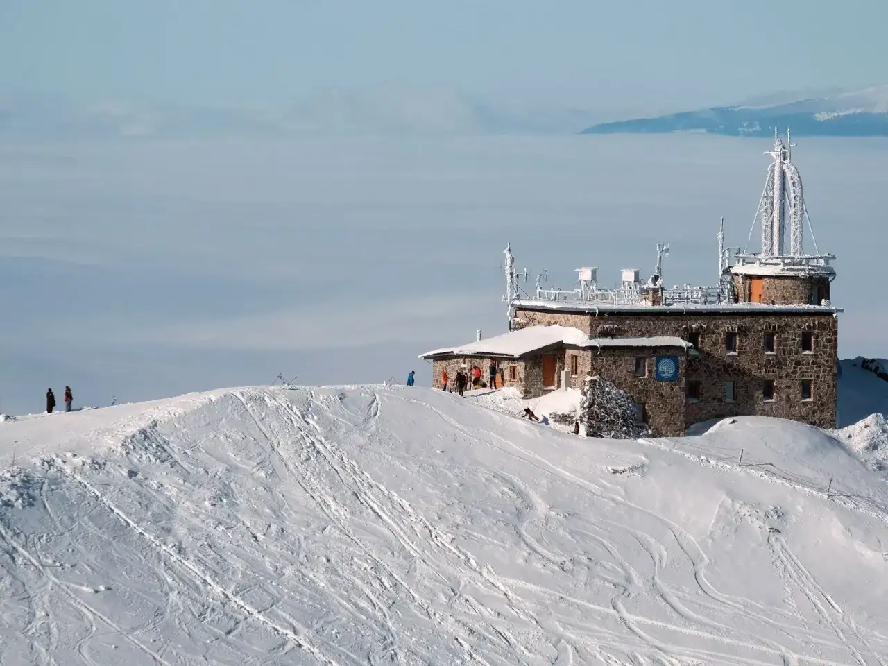 Kasprowy Wierch wysokość: kamienny budynek obserwatorium na ośnieżonym szczycie, otoczony chmurami i śladami nart.