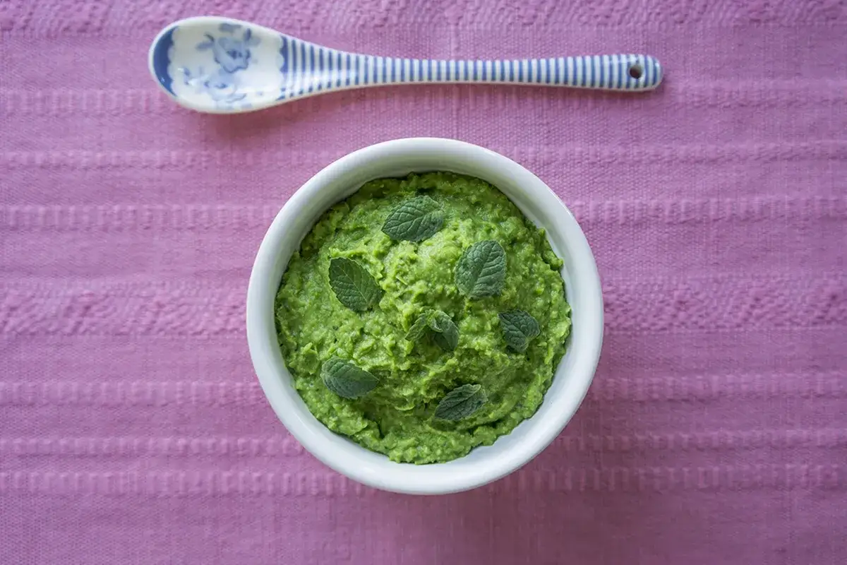 Pyszny, zielony groszek dla niemowlaka, udekorowany listkami mięty. Idealny pierwszy posiłek.