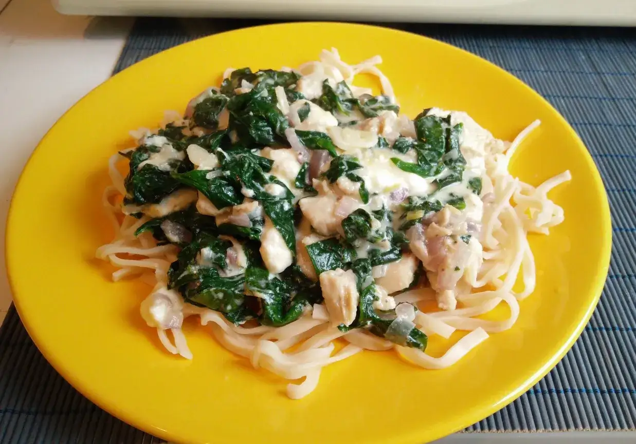Pyszny makaron ze szpinakiem i kurczakiem w kremowym sosie z fetą, podany na żółtym talerzu.