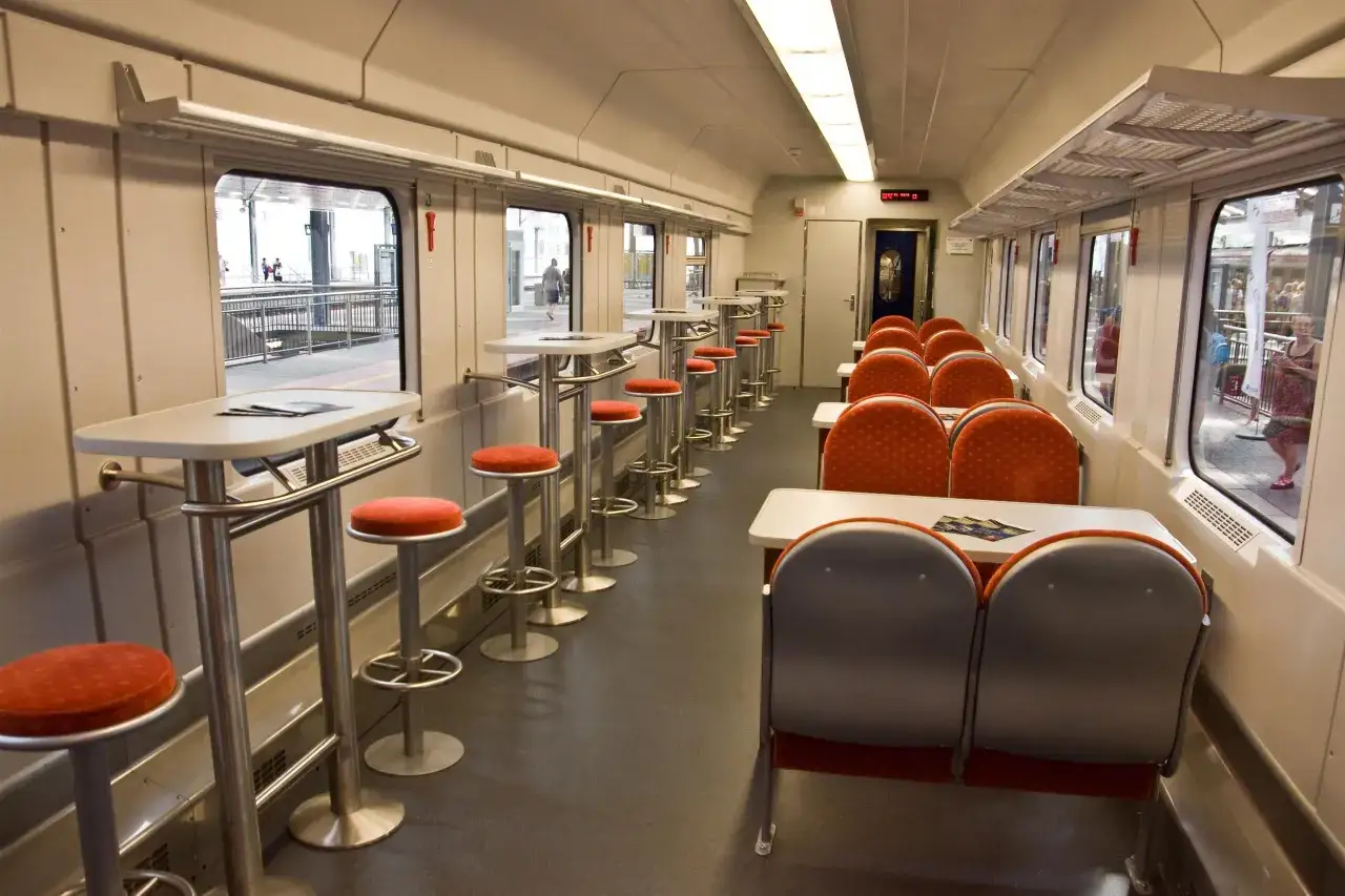 Wnętrze wagonu TLK z miejscami przy stolikach i siedzeniami. Czy w pociągu TLK jest wars? Tak, wygląda na to, że jest to wagon barowy.