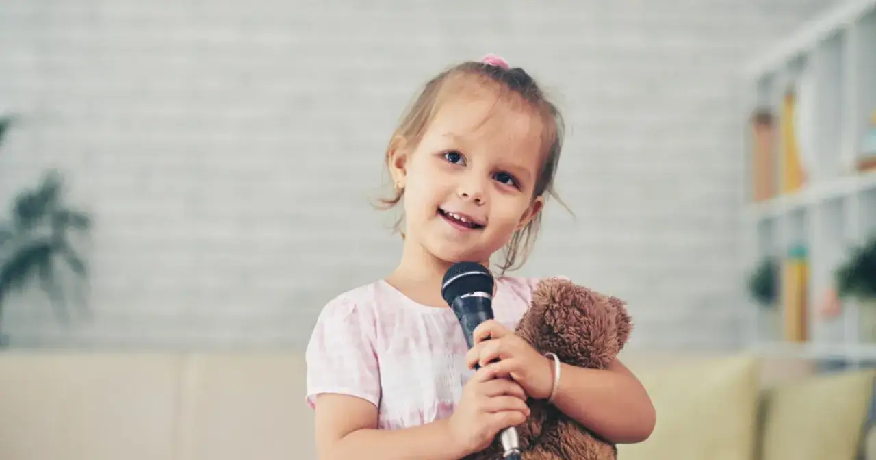 Uśmiechnięta dziewczynka z misiem i mikrofonem. Jej pewność siebie i radość to mocne strony dziecka, przykłady talentu.