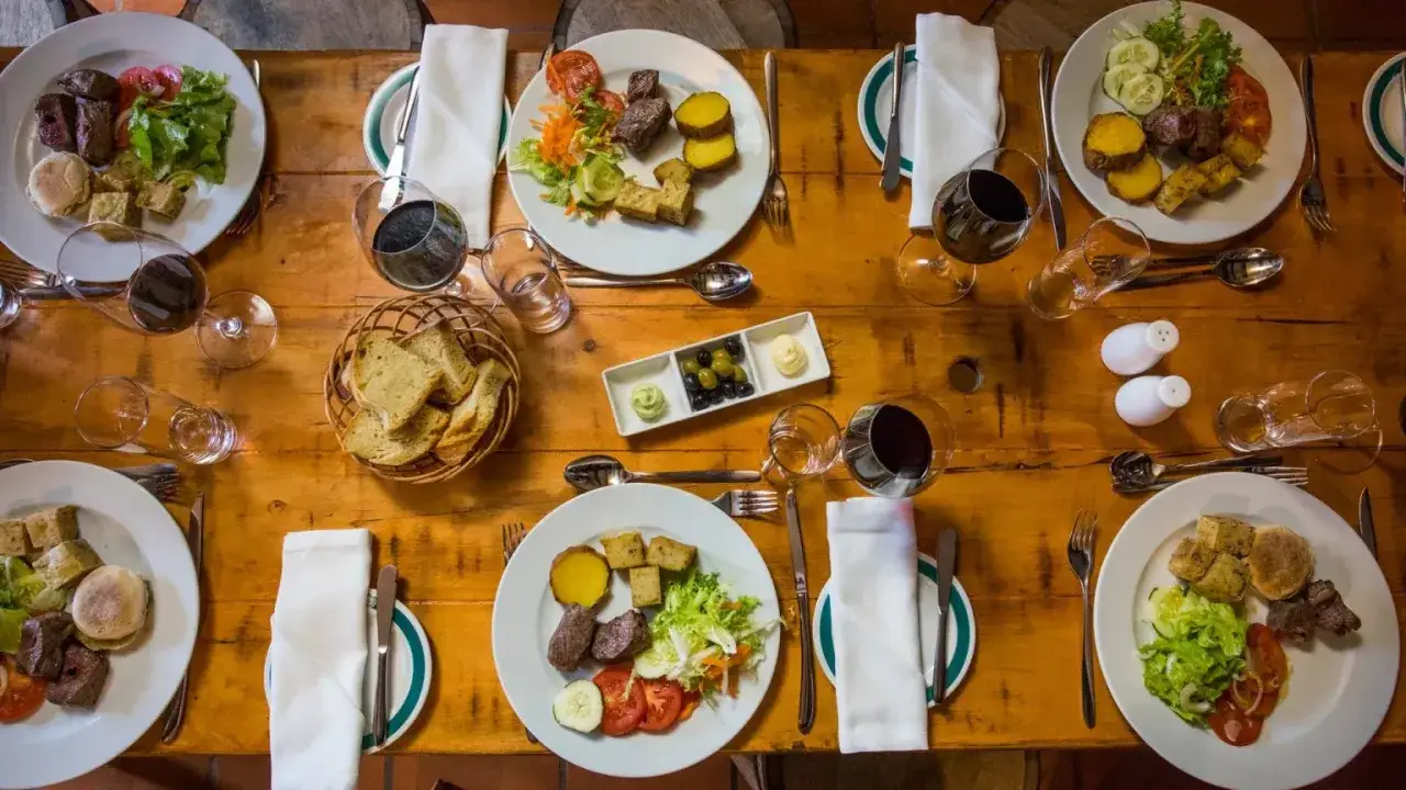 Na stole zastawionym daniami z mięsem, ziemniakami i sałatką, koszyk z pieczywem i oliwki. Idealne pomysły, co przywieźć z Maderze do jedzenia.