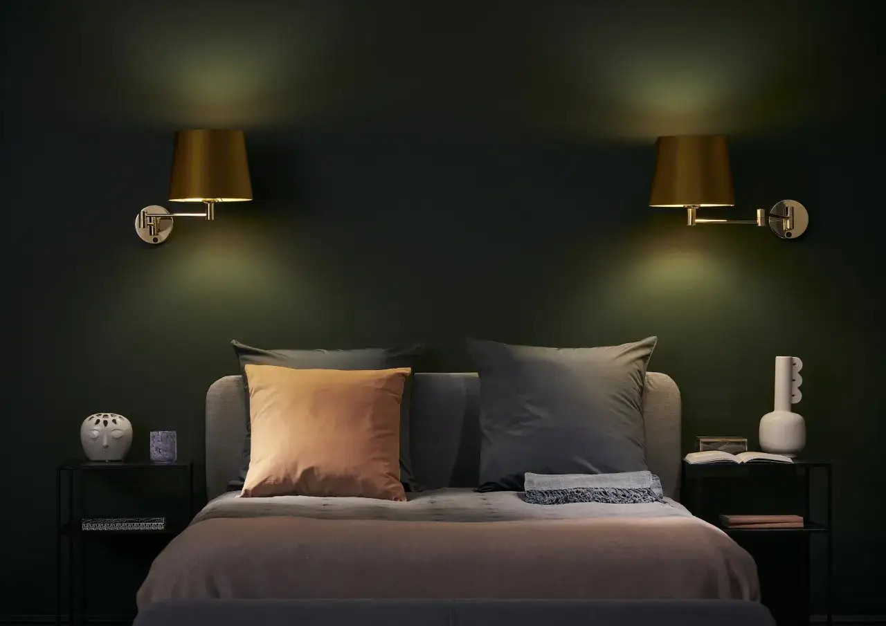 Eleganckie kinkiety do sypialni nad łóżko tworzą przytulną atmosferę. Po bokach łóżka stoją stoliki nocne z dekoracjami.