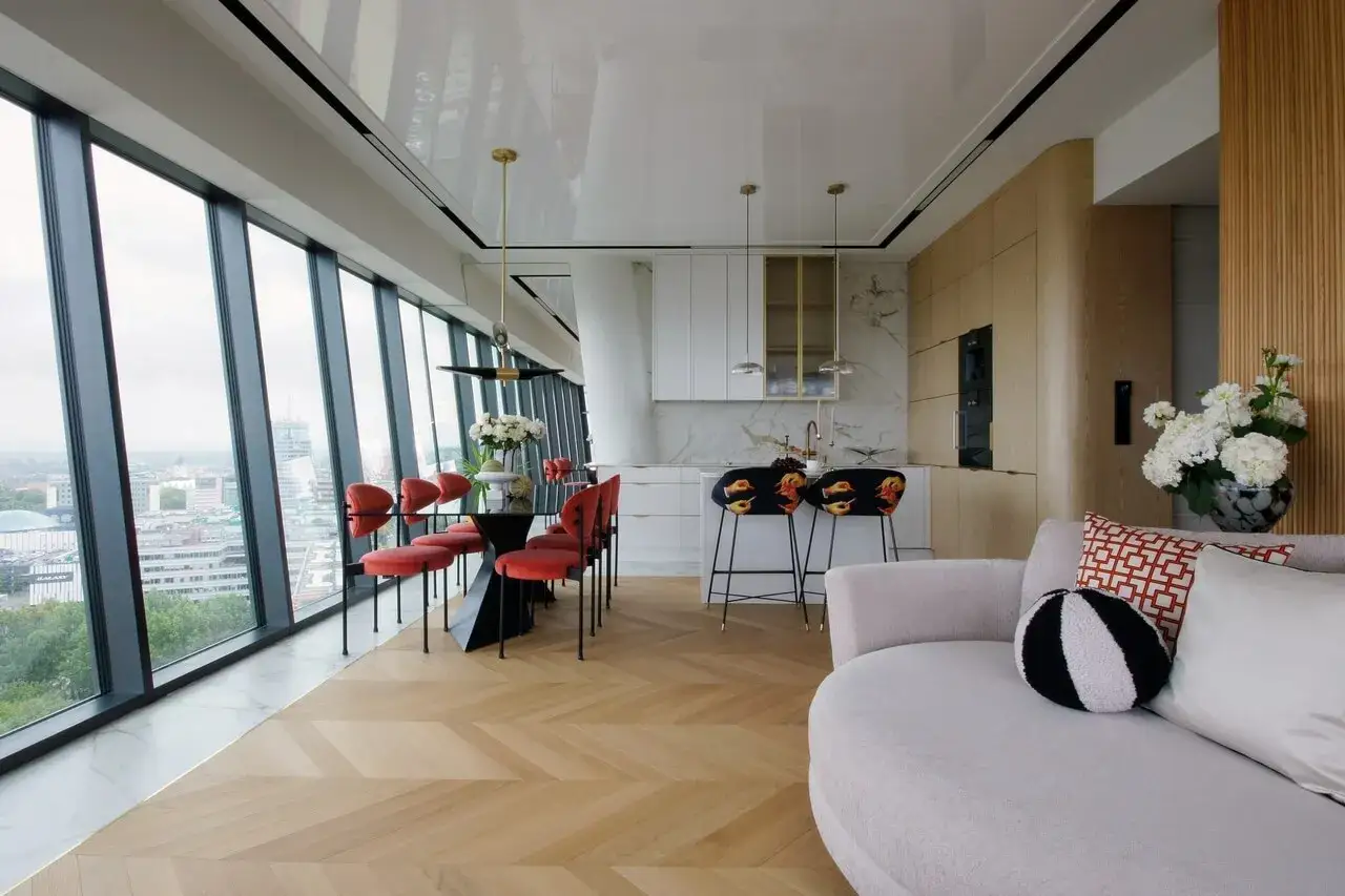Nowoczesne wnętrze z widokiem na miasto z okien hanza tower. Czerwone krzesła przy czarnym stole, kuchnia z wyspą i wygodna sofa.