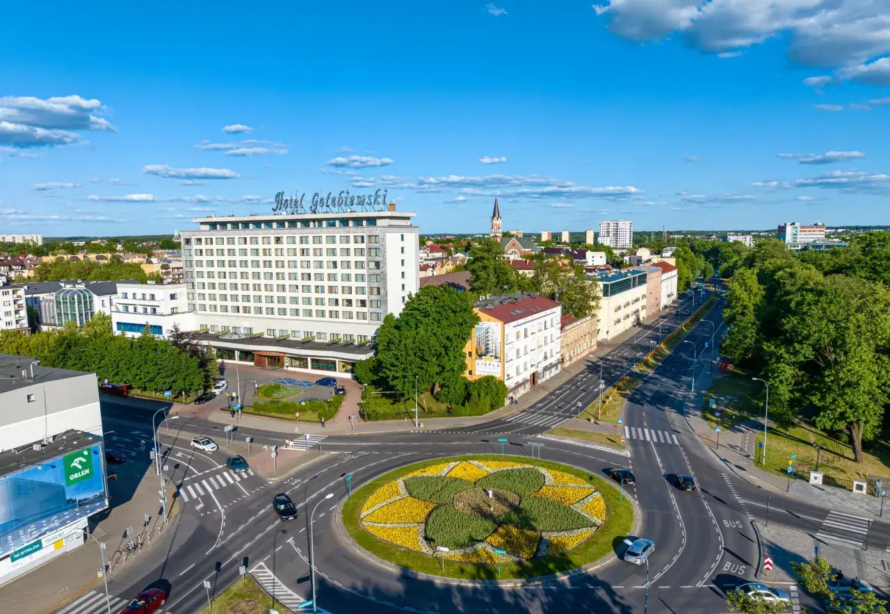 Hotel Gołębiewski w Białymstoku, otoczony zielenią i miejskim ruchem, stanowi centralny punkt tej panoramy.