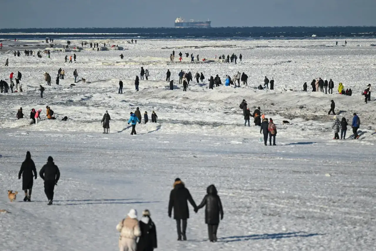 Ludzie spacerują po zamarzniętym Bałtyku, przypominając czasy, kiedy ostatnio zamarzło morze bałtyckie. Na horyzoncie widać statek.