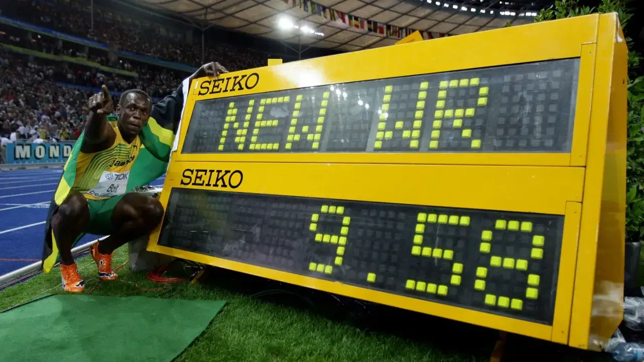 Usain Bolt z flagą Jamajki obok tablicy wyników z napisem 