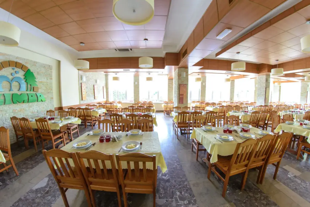 Jadalnia w sanatorium uzdrowiskowym Limba. Drewniane stoły i krzesła, nakryte żółtymi obrusami, czekają na gości.