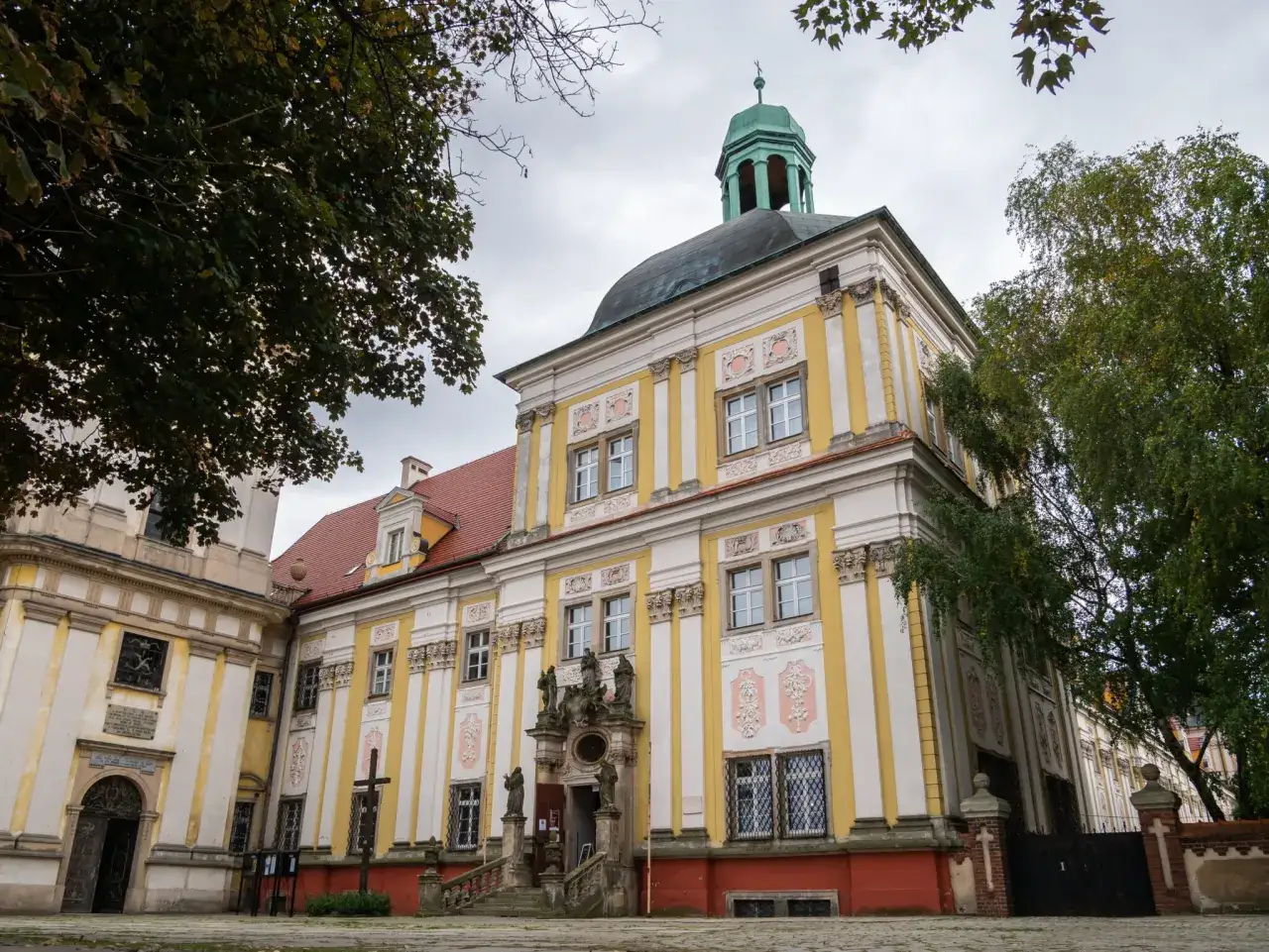 Barokowy pałac w Trzebnicy, z zieloną kopułą i ozdobnymi fasadami, to jedna z gł&oacute;wnych atrakcji miasta.