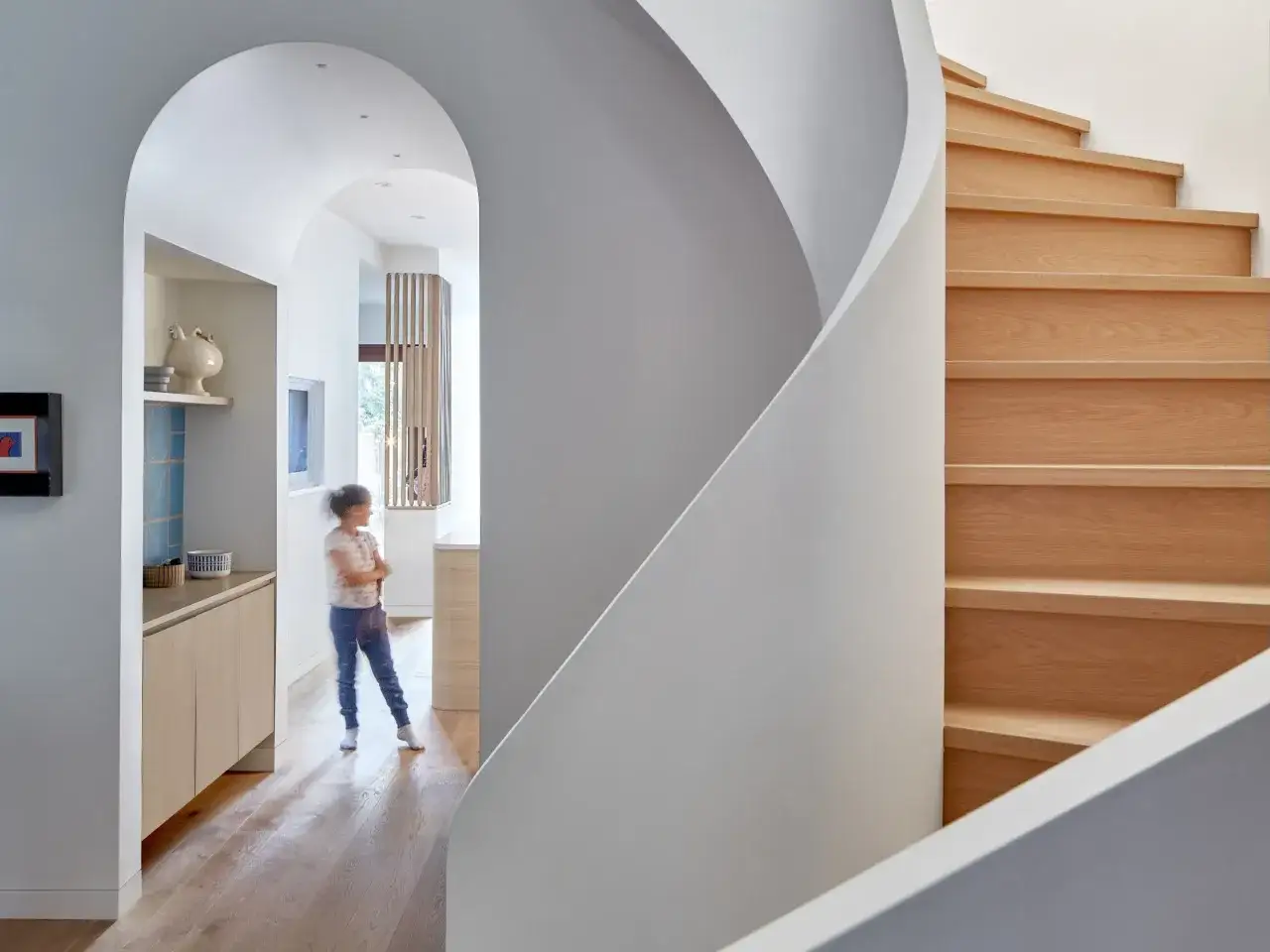 Nowoczesny salon z łukiem wykończonym gładką, białą ścianą, obok drewnianych schod&oacute;w.