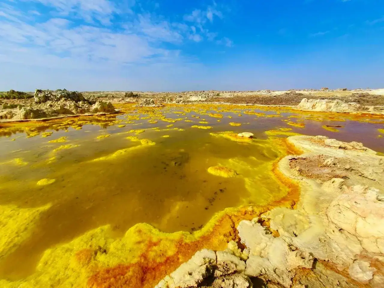 Ż&oacute;łte, mineralne osady otaczają gorące źr&oacute;dła w Kotlinie Danakilskiej. Niebo błękitne, chmury białe.