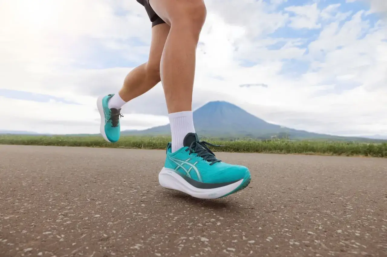 Biegacz w turkusowych butach Asics na tle g&oacute;ry.