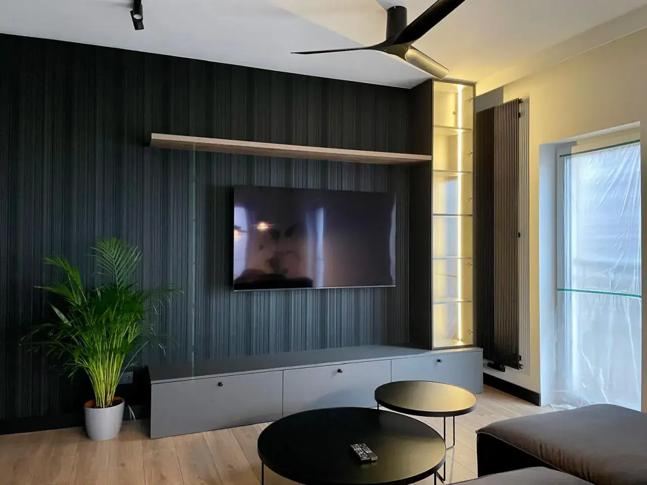 Nowoczesny salon z czarną tapetą, szarym RTV i podświetlaną witryną. Idealne pakiety wykończenia pod klucz.