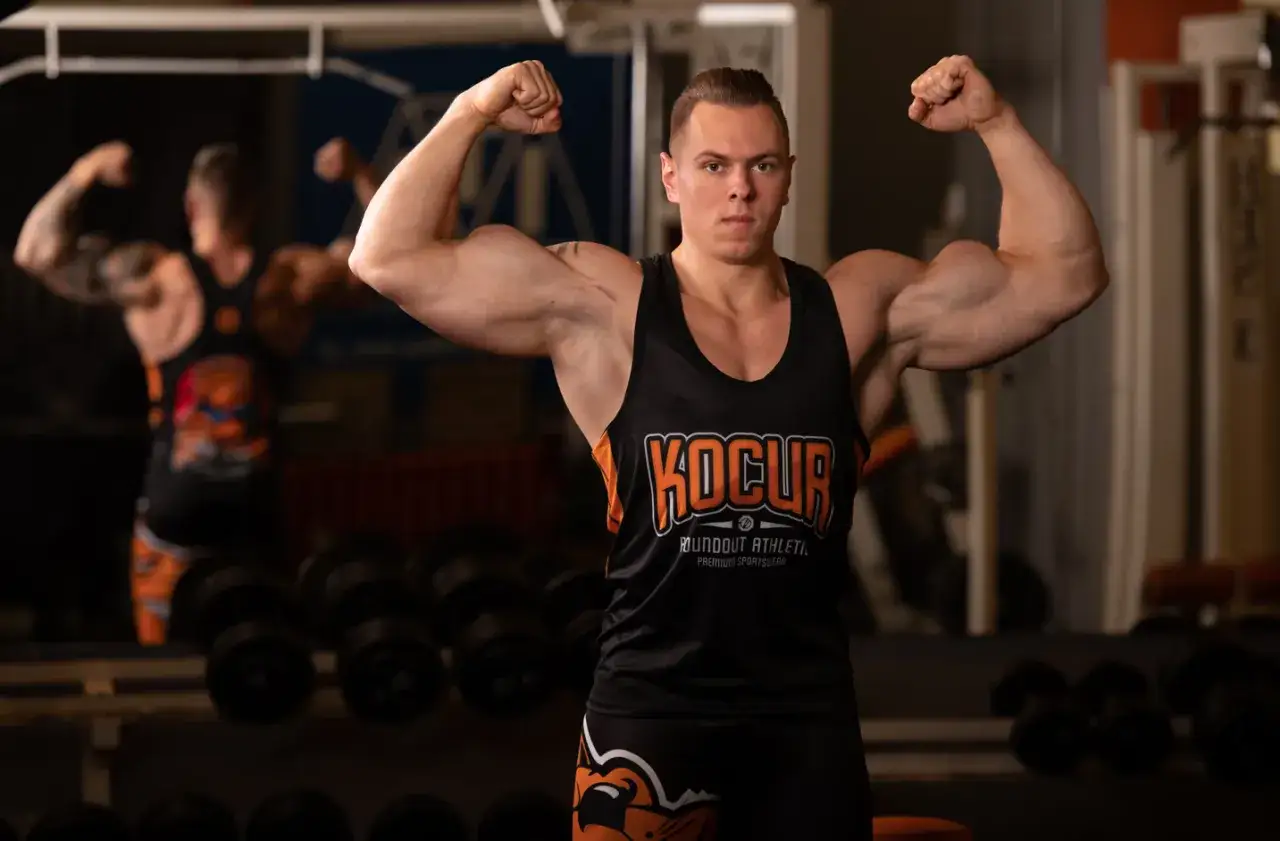Mężczyzna na siłowni napina bicepsy. Chcesz wiedzieć, jak szybko przytyć? Trening i odpowiednia dieta to klucz do sukcesu.