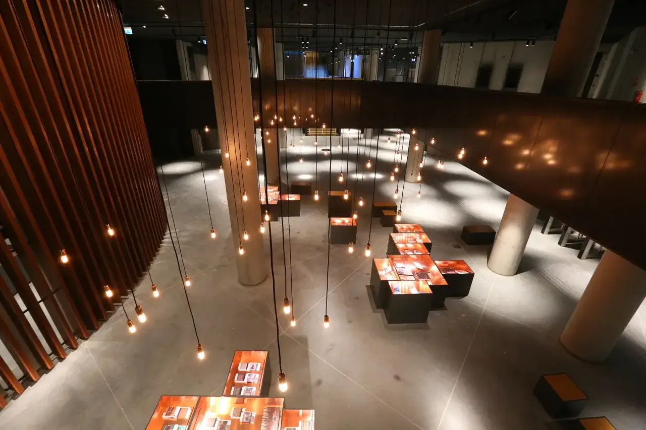 Wnętrze Muzeum II Wojny Światowej w Gdańsku, z wiszącymi żarówkami i nowoczesnymi ekspozycjami. Wiele osób poleca to miejsce.