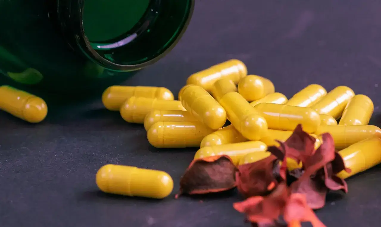 Ż&oacute;łte kapsułki berberyny wysypane z zielonego pojemnika. Zastanawiasz się nad berberyna skutki uboczne?