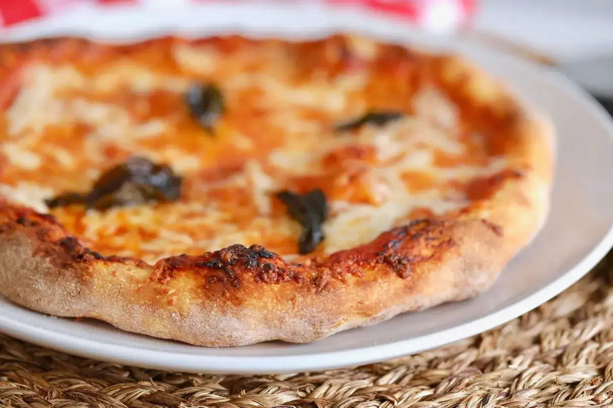 Puszyste ciasto na pizzę z ciągnącym się serem i aromatycznymi listkami bazylii, gotowe do zjedzenia.