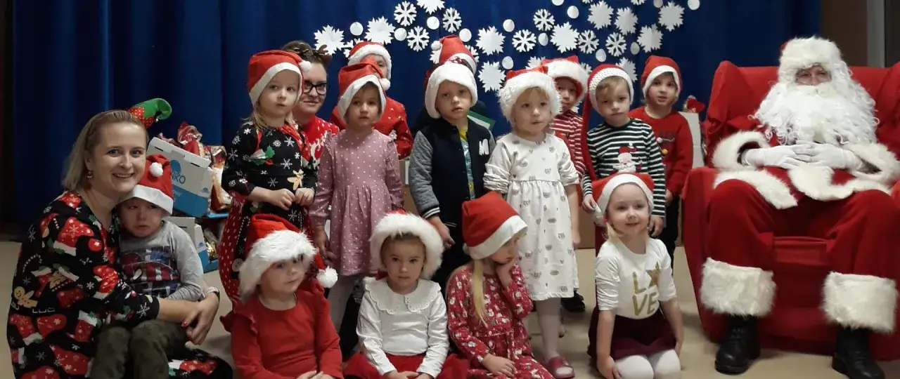 Dzieci w czapkach Mikołaja i pani z prezentami. Wspaniałe mikołajki klasowe pomysły na wsp&oacute;lne świętowanie.