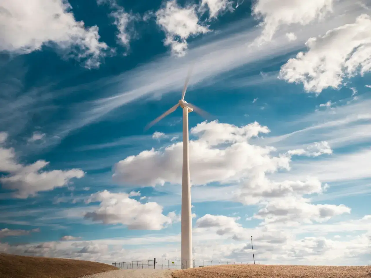 Wiatrak na tle błękitnego nieba z chmurami. Symbol nowoczesnych zródeł energii odnawialnej, czerpiących moc z natury.