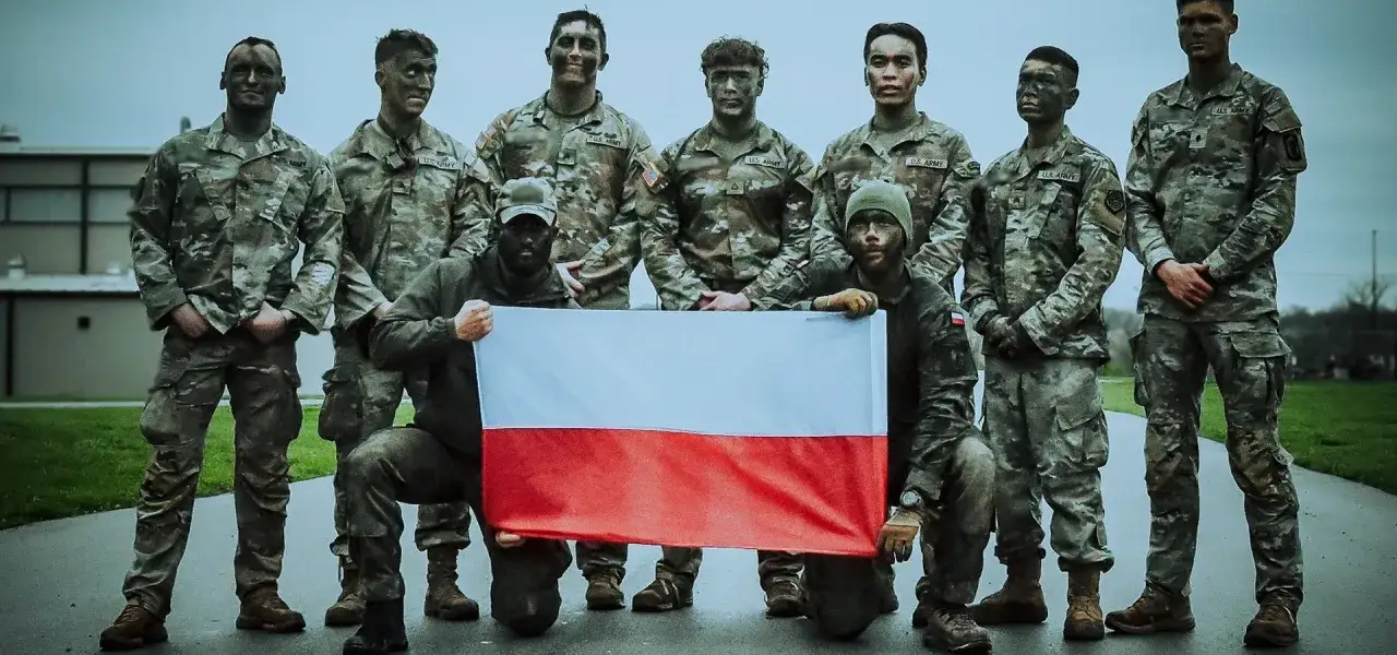 Grupa żołnierzy w mundurach, z twarzami pomalowanymi farbą maskującą, trzyma polską flagę. To inspiracja, jak wstąpić do wojska i służyć ojczyźnie.