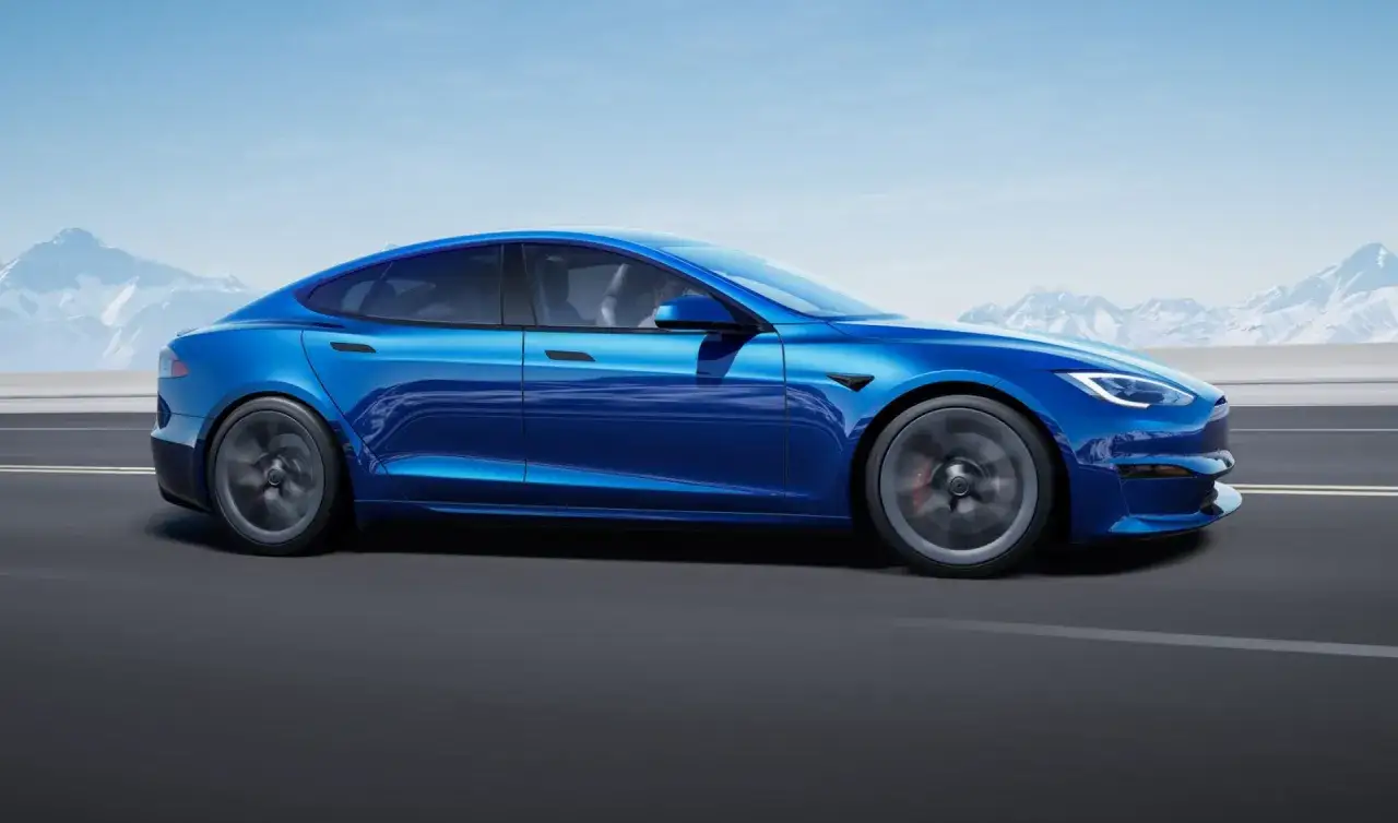 Błękitny Tesla Model S z imponującą mocą, pędzący po drodze z widokiem na ośnieżone g&oacute;ry.
