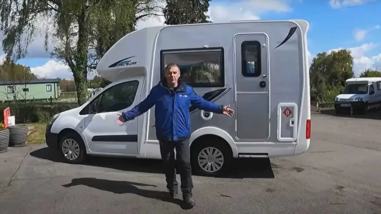 Mężczyzna prezentuje mały kamper z łazienką, idealny na wakacyjne wyprawy.