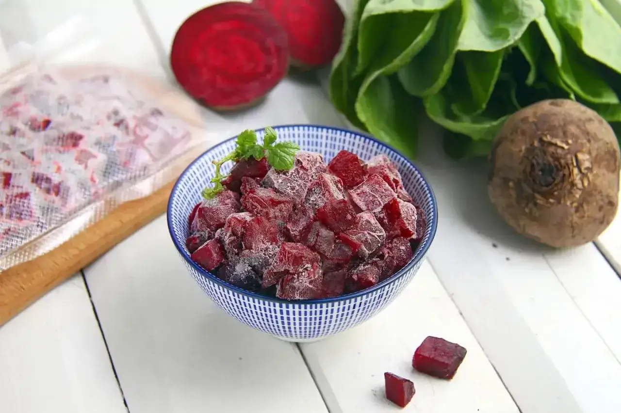 Mrożone kostki buraków w misce, obok świeżych buraków i liści. Odpowiedź na pytanie: czy można mrozić surowe buraki.
