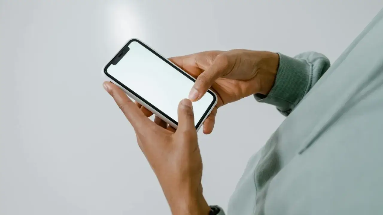 Dłonie trzymające iPhone'a, być może przygotowujące się do wykonania hard reset iPhone, aby rozwiązać problem.