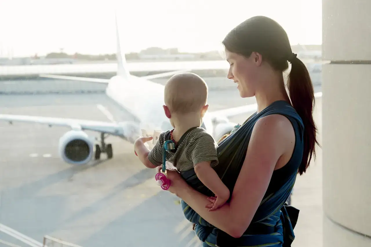 Mama z półrocznym dzieckiem w chuście na lotnisku, patrzą na samolot. Idealne miejsce, gdzie na wakacje z półrocznym dzieckiem.