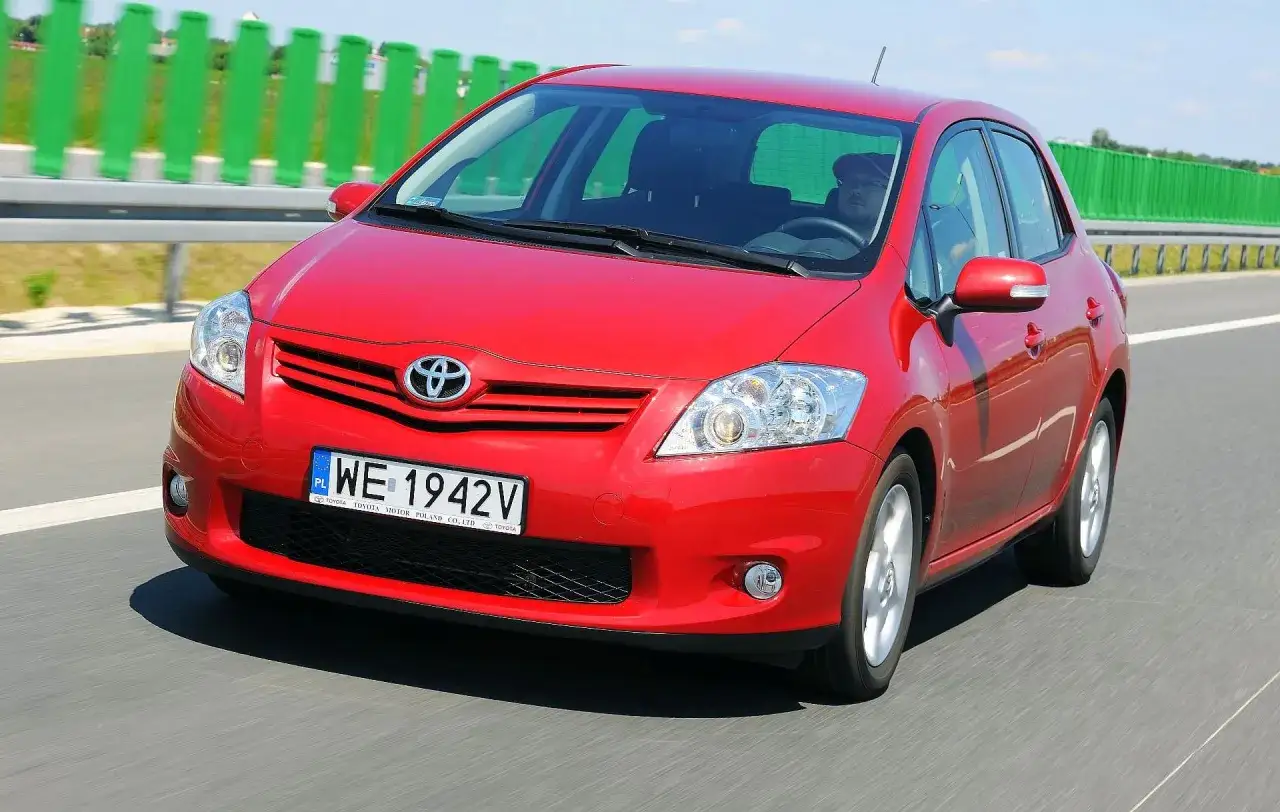 Czerwony Toyota Auris jedzie autostradą. Kierowca w czapce prowadzi auto.