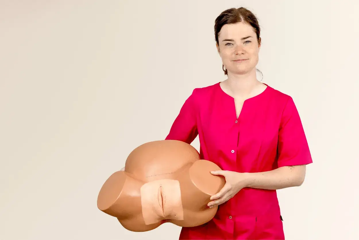 Kobieta w różowej bluzce trzyma model miednicy, pokazując jak wykonać masaż krocza.