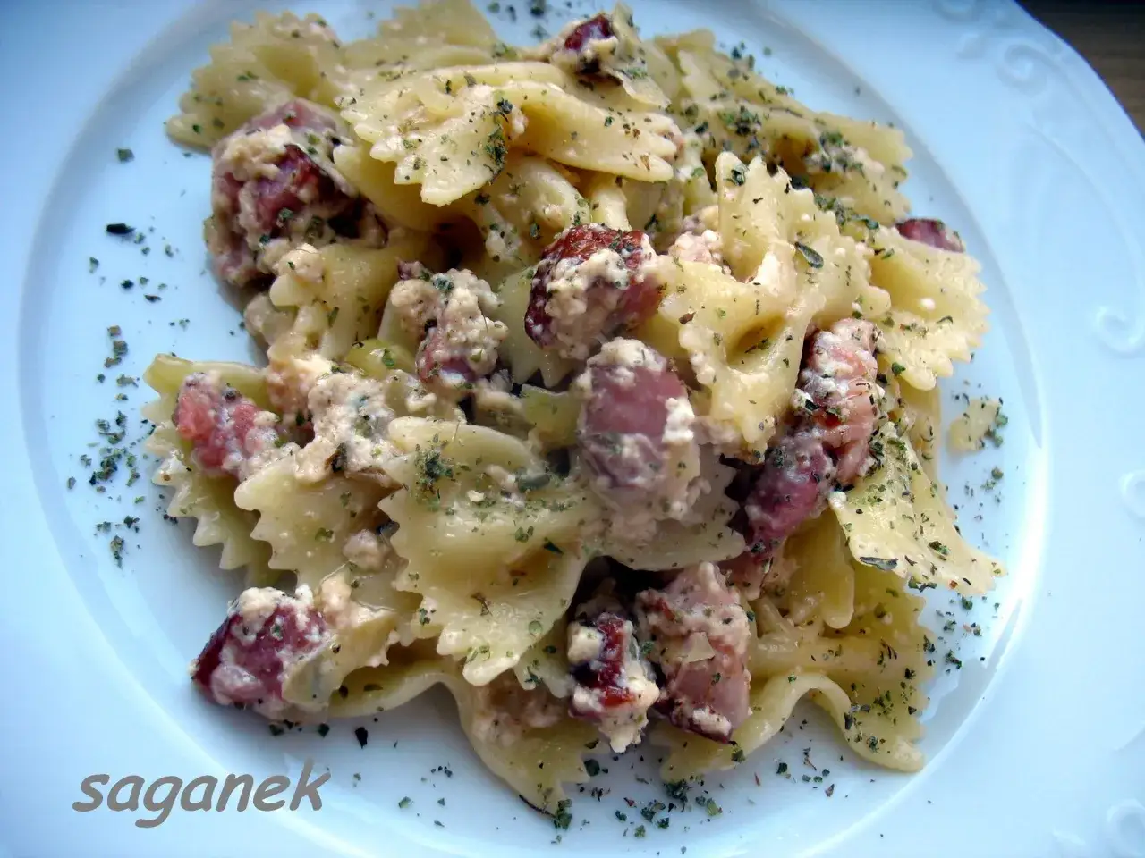 Pyszny makaron farfalle z kremowym twarogiem i kawałkami kiełbasy, posypany ziołami. Idealny na szybki obiad.