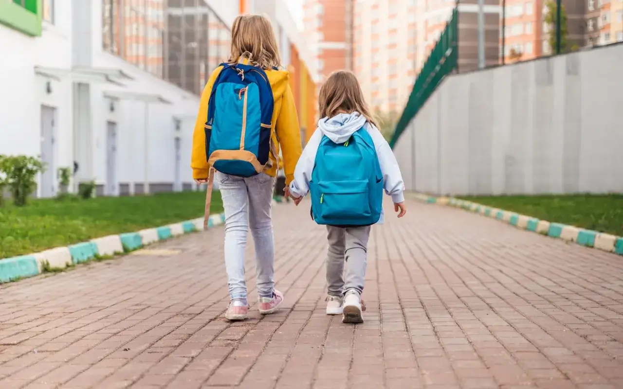Dwie dziewczynki z plecakami idą chodnikiem. Czy dzieci mogą wychodzić same? To pytanie zadaje sobie wielu rodziców.