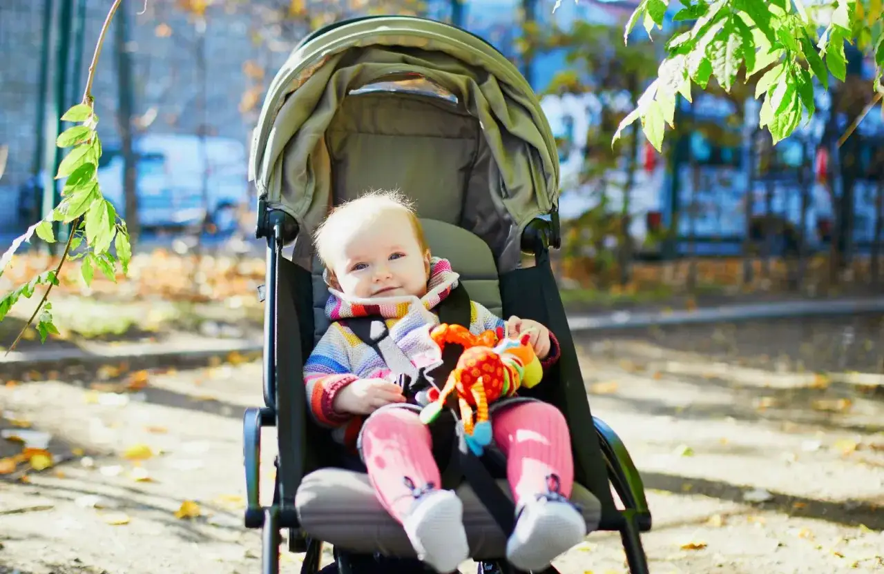 Uśmiechnięte dziecko w w&oacute;zku spacerowym, idealnym do jakiego wieku, bawi się kolorową zabawką.