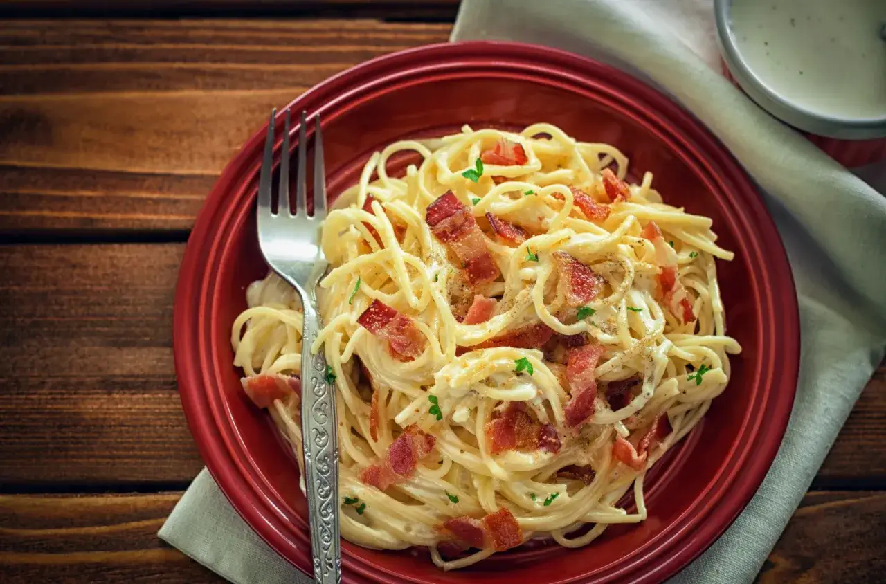 Pyszne spaghetti carbonara z chrupiącym boczkiem, posypane natką pietruszki. Idealne danie, gdy zastanawiasz się nad spaghetti carbonara kcal.