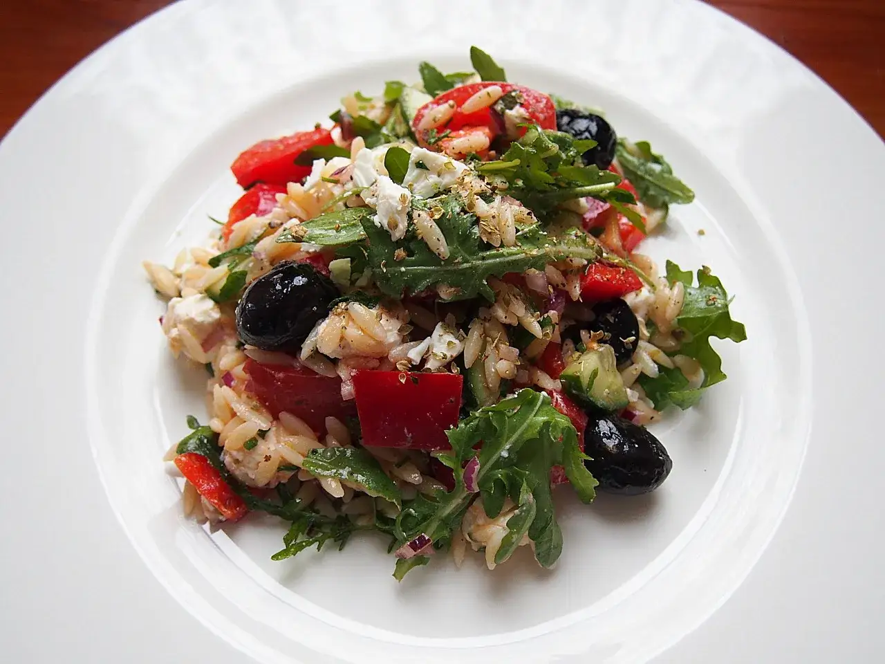 Kolorowa sałatka z makaronem orzo, oliwkami, fetą i rukolą, doprawiona ziołami. Pyszna i lekka.