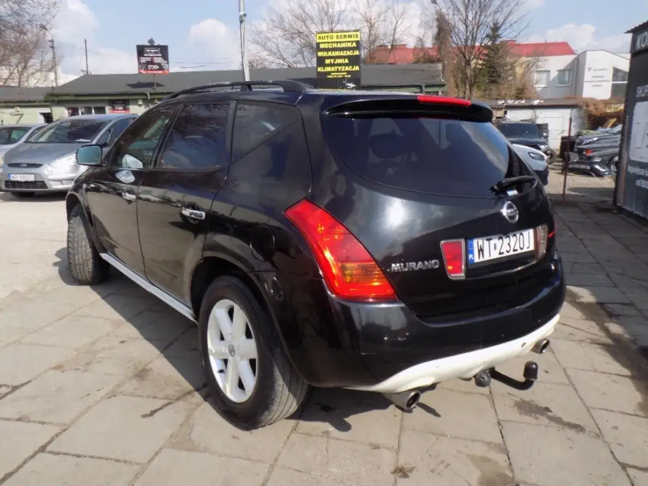 Czarny Nissan Murano 3.5 V6 z hakiem holowniczym i tablicą rejestracyjną WT-2320J stoi na parkingu.
