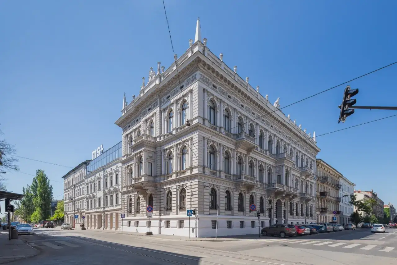 Elegancki budynek Muzeum Sztuki w Łodzi z secesyjną fasadą, otoczony ulicą i samochodami.