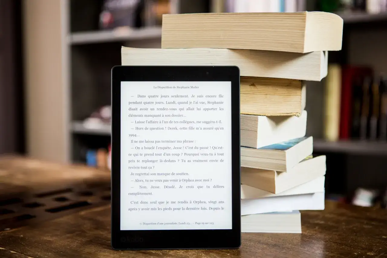 Mobi to czytnik e-booków obok stosu papierowych książek. Czytanie na ekranie jest wygodne, a książki zajmują mniej miejsca.
