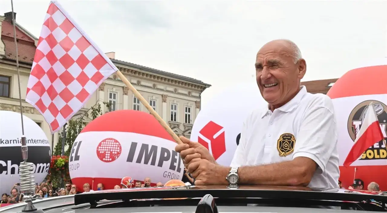 Uśmiechnięty mężczyzna z flagą w kratkę. W tle balony i budynki. Co się stało Langowi?