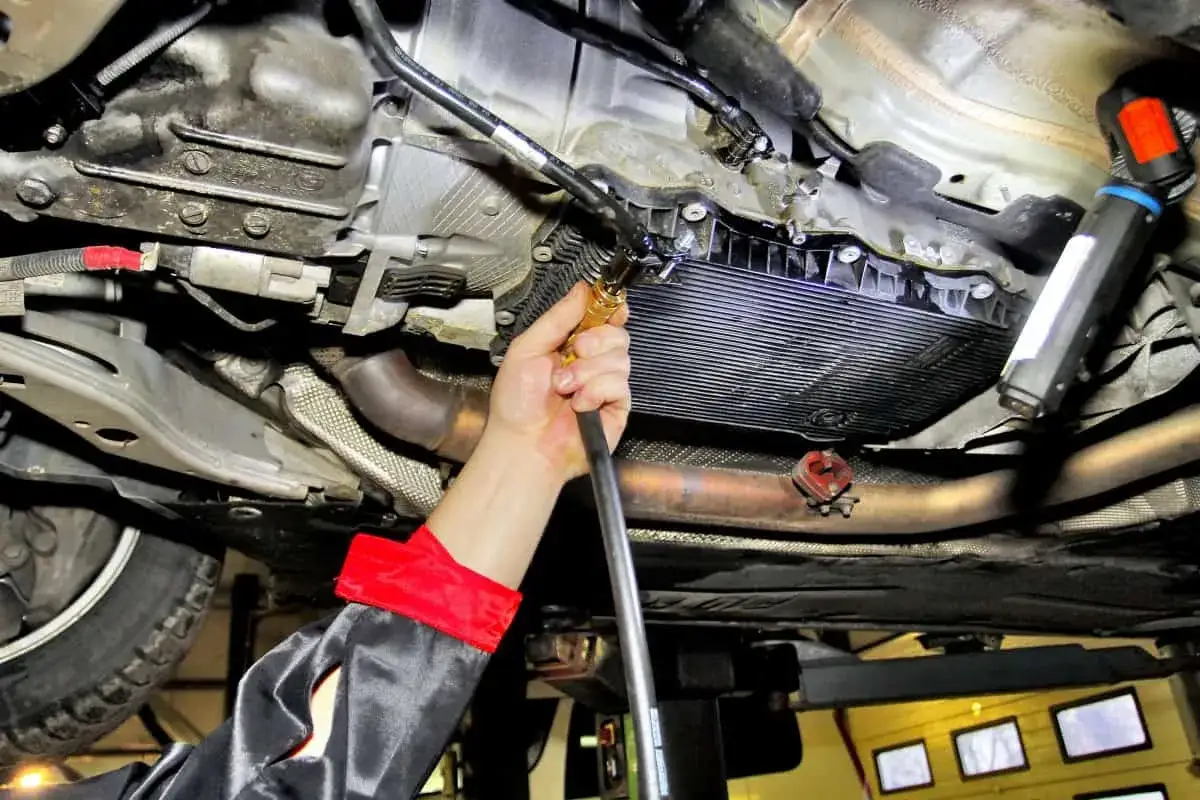 Mechanik wykonuje wymianę oleju w skrzyni automatycznej, używając węża do spuszczenia płynu.