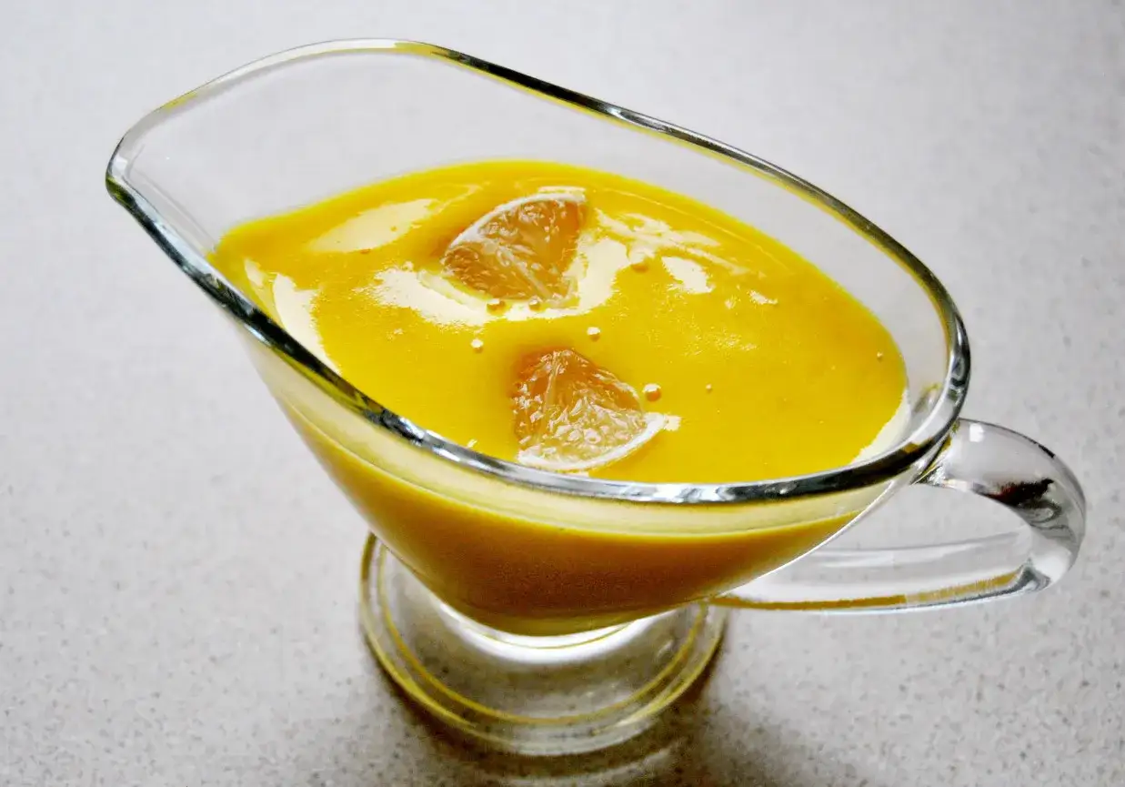 Pyszny, ż&oacute;łty sos cytrynowy do ryby, ozdobiony kawałkami cytryny, w szklanej sosjerce.