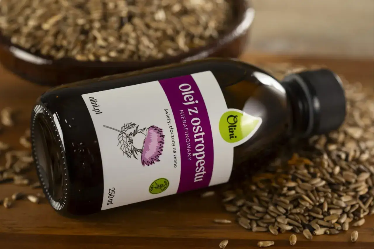 Butelka oleju z ostropestu, kt&oacute;ry może przynieść wspaniałe olej z ostropestu na twarz efekty. W tle nasiona ostropestu.