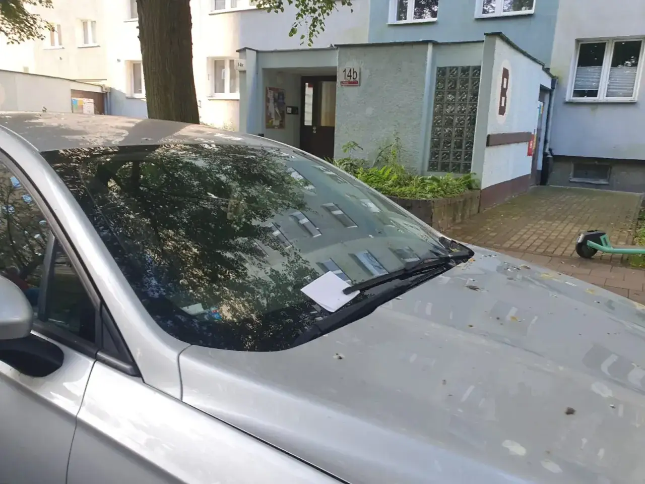 Biała kartka pod wycieraczką samochodu, prawdopodobnie mandat za parkowanie na terenie wspólnoty mieszkaniowej.