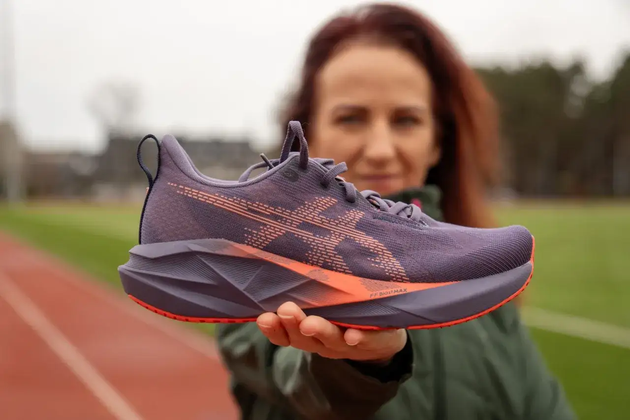Kobieta prezentuje fioletowe buty do biegania Asics z pomarańczowymi akcentami, gotowa na trening.