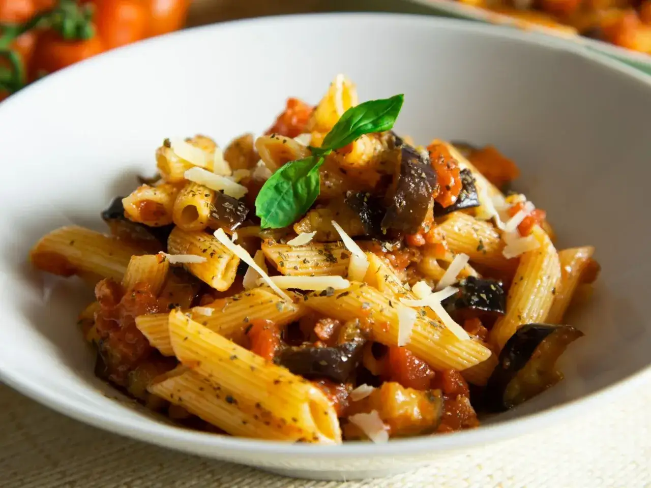 Pyszne rigatoni alla norma z bakłażanem, pomidorami i parmezanem, udekorowane bazylią.
