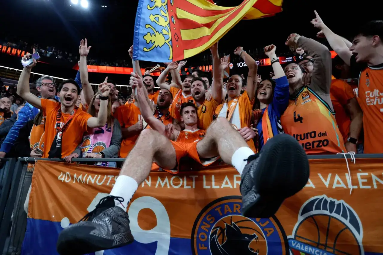 Aficionados celebran eufóricos una victoria en la Europa League de baloncesto. Un jugador es levantado por la multitud.