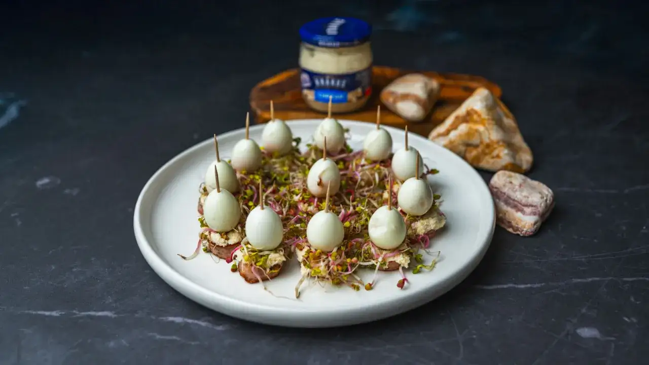 Eleganckie przystawki na Wielkanoc: małe jajka przepiórcze na kiełkach z pastą, podane na talerzu.